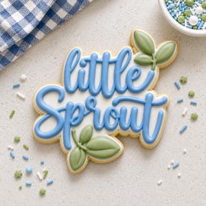 May include: A sugar cookie shaped like the words little Sprout in blue icing on a white base. The cookie features two green leaf accents, one at the top right and one at the bottom left, with a smooth finish and raised lettering details.
