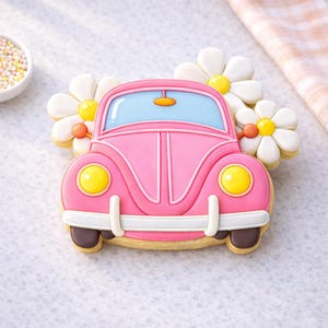 May include: A pink car-shaped cookie with yellow headlights and a blue windshield. The cookie is decorated with white and yellow daisy cookies. The car has brown tires and a white bumper. A small bowl of sprinkles is in the background.