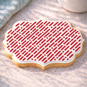 May include: A decorative cookie with a white border and a red pattern of diagonal lines and dots. The cookie has a light brown, slightly scalloped edge, and is likely a sweet treat.