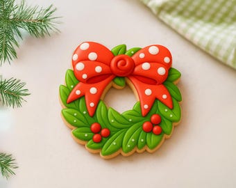 May include: A Christmas wreath cookie with a red bow featuring white polka dots. The wreath is made of green leaves with red berries and white accents. The cookie has a light brown edge.