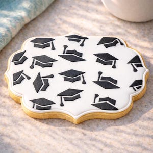 May include: A decorated sugar cookie with a white base and black graduation cap designs. The cookie has a scalloped edge and a light brown colour. The cookie is a celebratory treat for graduation.
