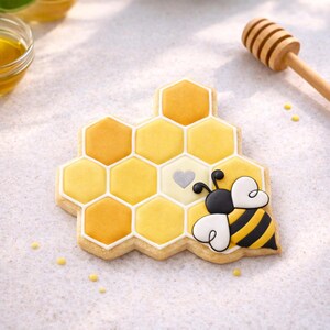 Puede incluir: Una galleta decorada con forma de panal de abejas con una abeja. El panal es amarillo y naranja con un contorno blanco. La abeja tiene rayas negras y amarillas y alas blancas en forma de corazón. Un palito de miel de madera está en el fondo.