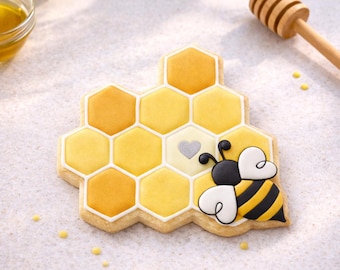 May include: A decorated sugar cookie shaped like a honeycomb with a bee. The honeycomb is yellow and orange with a white outline. The bee has black and yellow stripes and white heart-shaped wings. A wooden honey dipper is in the background.