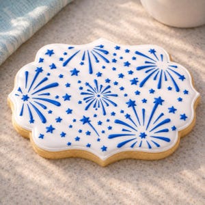 May include: A decorated sugar cookie with white icing and blue firework and star designs. The cookie has a scalloped edge and a light brown colour. The cookie is a sweet treat.