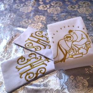 May include: Three white fabric altar cloths with gold embroidery. The centre cloth features a depiction of Jesus washing the feet of a disciple. The other two cloths have the letters "HH" embroidered in a decorative script.