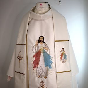 May include: White liturgical vestment with gold embroidery of Jesus Christ with a red and blue heart. The embroidery is of the Divine Mercy image.