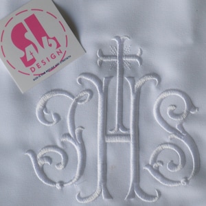 Op de afbeelding: Wit geborduurd monogram met de letters "IHS" en een kruis boven de letters. De letters zijn in een traditioneel schrift.