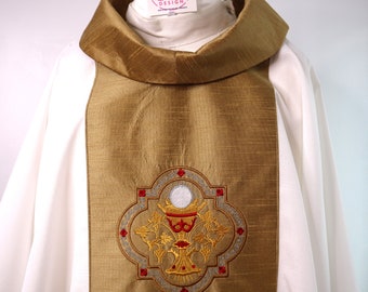 May include: White liturgical vestment with a gold stole featuring an embroidered chalice and host design. The stole has a decorative border with red and silver accents.