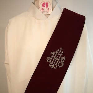 May include: A burgundy stole with a silver embroidered IHS monogram. The stole is worn over a white clerical shirt.