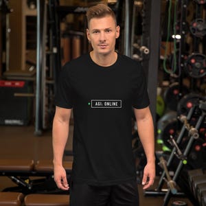 May include: A black short-sleeved t-shirt featuring a white rectangular graphic on the chest. Inside the rectangle, the text reads AGI: ONLINE in a clean, sans-serif font, accompanied by a small green dot positioned to the left of the text.