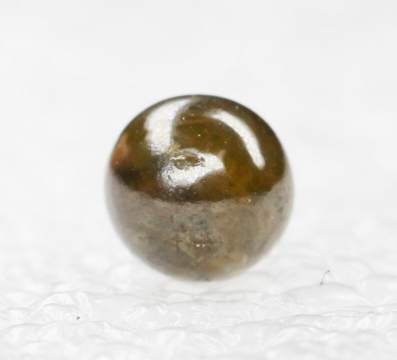 Puede incluir: Una gema redonda de color verde oscuro con una superficie brillante y reflectante.