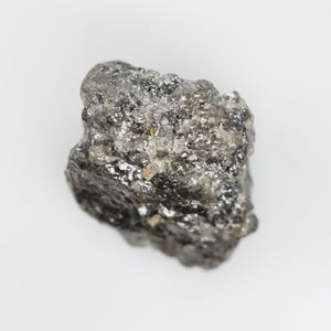 Puede incluir: Un cristal de diamante en bruto, gris y negro, con un acabado natural sin pulir.