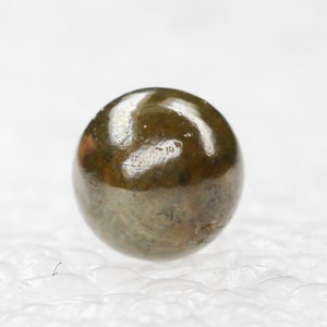 Puede incluir: Una sola gema redonda de color verde oscuro con una superficie brillante y pulida.