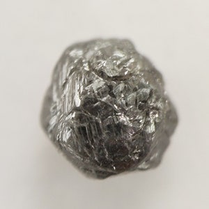 May include: A rough, gray, octahedral diamond crystal. The crystal is faceted and has a metallic sheen.