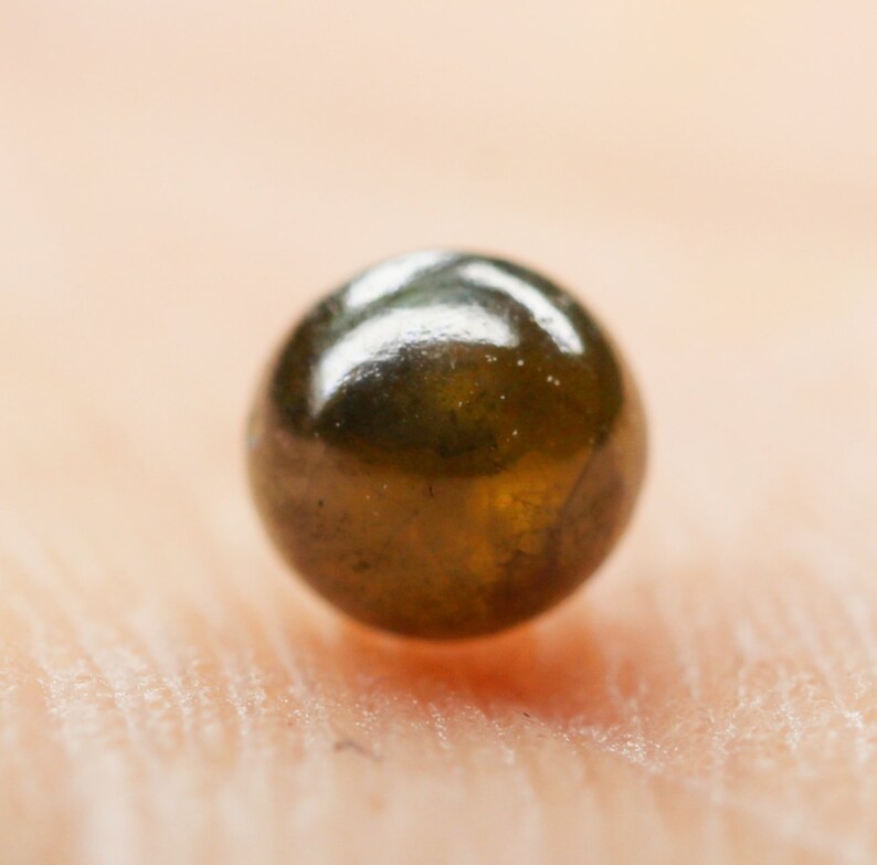 Puede incluir: Primer plano de una cuenta redonda de color verde oscuro con una superficie brillante y reflectante.