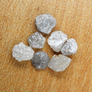 Peut inclure: Une collection de sept diamants bruts non taillés de différentes tailles et formes. Les diamants sont un mélange de gris et de blanc et ont une apparence naturelle non polie.