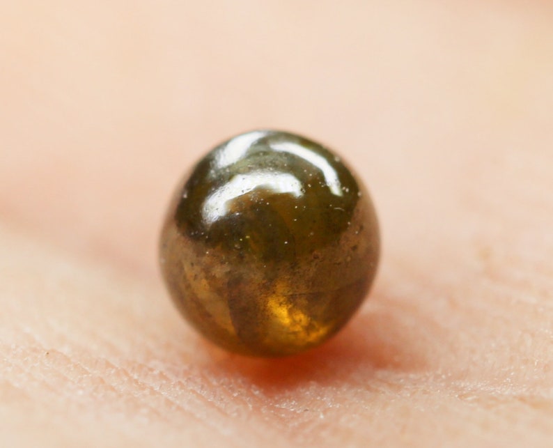 Puede incluir: Una sola cuenta redonda de color verde oscuro y marr&oacute;n con una superficie brillante y reflectante.