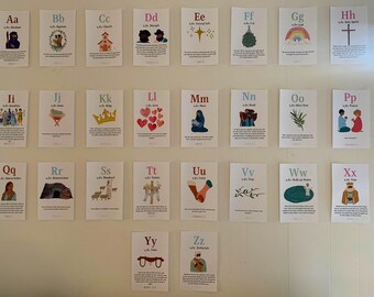 May include: A collection of 26 small cards, each featuring a letter of the alphabet with an accompanying illustration and text. The cards are arranged on a white wall. The illustrations include a church, a rainbow, and a crown.