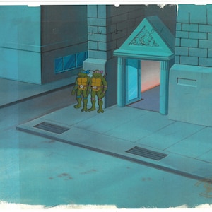 May include: Two green and brown Teenage Mutant Ninja Turtles stand in front of a building with a doorway. The building is made of brick and has a stone archway above the doorway. The turtles are wearing their signature masks and bandanas.