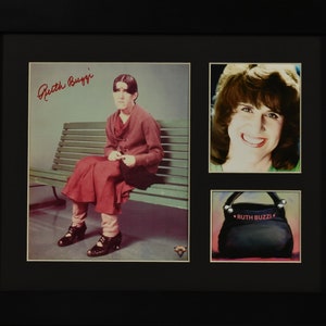 May include: A framed collage of photos featuring a woman in a red dress sitting on a bench, a close-up of the woman's face, and a black handbag with the text "Ruth Buzzi" in pink.