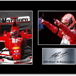 Könnte beinhalten: Gerahmter Druck mit zwei Bildern von Michael Schumacher: eines in einem roten Formel-1-Auto, das andere beim Feiern. Eine silberne Plakette darunter zeigt seine Unterschrift und seinen Namen. Der Druck ist vor einem schwarzen Hintergrund.