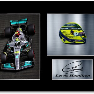 Könnte beinhalten: Gerahmter Druck mit einem Formel-1-Rennwagen, einem gelb-blauen Rennhelm und der Unterschrift von Lewis Hamilton. Das Auto ist silber und türkis. Der Helm hat Sponsorenlogos.
