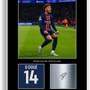 Pode incluir: Impressão emoldurada com um jogador de futebol em uma camisa azul marinho com detalhes em vermelho e branco, celebrando em um campo verde. Inclui um gráfico de camisa com "D. Doué" e o número "14".