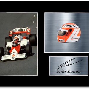 Könnte beinhalten: Gerahmter Druck mit einem Formel-1-Rennwagen mit Marlboro-Branding, einem Rennhelm mit Parmalat- und Marlboro-Logos und einer Unterschrift von Niki Lauda. Das Auto ist weiß und rot.