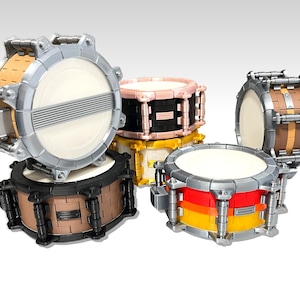 Pode incluir: Cinco baterias de tambor de diferentes cores feitas de blocos de Lego. Os tambores estão empilhados uns sobre os outros. Os tambores são todos de cores diferentes e têm designs diferentes.