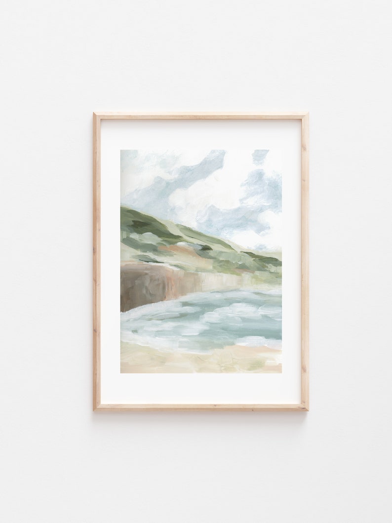 May include: Abstract landscape art print in a natural wood frame. The artwork features a coastal scene with green hills, a sandy beach, and a light blue sky with clouds. The painting uses a brushstroke style with muted colors.