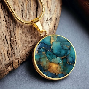 May include: A gold-colored necklace with a round pendant. The pendant features a turquoise and gold-colored stone with a cracked pattern. The necklace is displayed on a piece of wood.