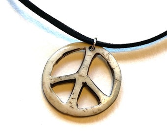 May include: A white peace sign pendant necklace with a black suede cord.