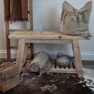 May include: A wooden bench with a rolled blanket and a decorative bird ornament. A brown blanket with a fringed edge hangs on a wooden ladder. A framed black and white print with the word "chill" is on the wall.