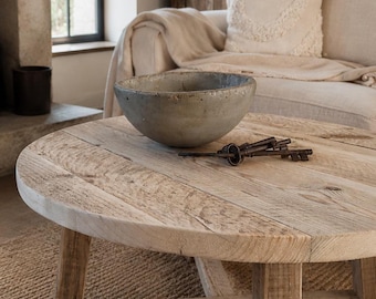 Puede incluir: Una mesa de centro redonda de madera con acabado marrón claro y base en cruz. Un cuenco circular gris y desgastado se encuentra sobre la mesa junto a un pequeño grupo de tres llaves antiguas de metal oscuro y oxidado sobre la madera.
