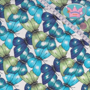 Könnte beinhalten: Weißer Stoff mit einem sich wiederholenden Muster aus blauen und grünen Schmetterlingen. Der Stoff hat ein Maßband darauf mit dem Text "feenkleid design".