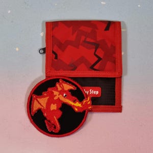 Könnte beinhalten: Rotes und schwarzes Portemonnaie mit einem passenden Drachenaufnäher. Das Portemonnaie hat ein rotes Tarnmuster und ein schwarzes Innenfutter. Der runde Drachenaufnäher zeigt einen roten Drachen mit orangefarbenen Flügeln auf schwarzem Hintergrund. Das Portemonnaie hat den Text "by Step".