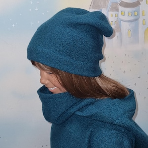 Puede incluir: Un gorro de lana azul turquesa y un jersey de cuello alto a juego. El gorro es holgado y el jersey tiene un corte amplio y holgado.