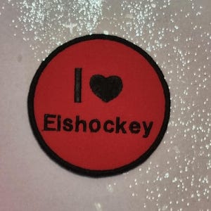 Puede incluir: Parche circular de fieltro rojo con texto bordado en negro que dice "Me encanta el hockey sobre hielo".