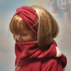 May include: A young girl wearing a red fleece hooded jacket with a white trim. She is wearing a red fleece headband with a twist detail.