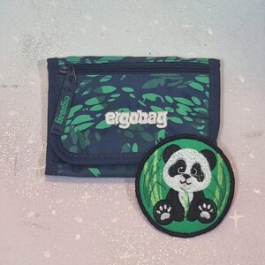 Könnte beinhalten: Eine marineblau und grün gemusterte Geldbörse mit dem Markennamen "ergobag" und einem passenden runden Aufnäher. Der Aufnäher zeigt ein Panda-Bären-Design mit grünem Hintergrund.