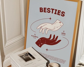 May include: A light blue poster with the text "BESTIES" in red lettering. Two hands are depicted, one white and one red, with constellations representing the zodiac signs Virgo and Gemini. The text "ELIZABETH VIRGO" and "ROSE GEMINI" are below the hands. The poster is framed in a light wood frame.