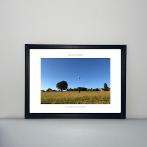 May include: A framed print of Bathwick Meadow, featuring a vibrant field under a clear blue sky. A hot air balloon floats in the distance. The print is in a black frame.