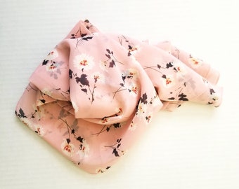 Op de afbeelding: Een roze, doorschijnende sjaal met een bloemenprint. De bloemen zijn wit met bruine stelen en bladeren.