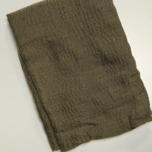 K&ouml;nnte beinhalten: Ein rechteckiges St&uuml;ck Stoff in einem einfarbigen Olivgr&uuml;n. Das Textil weist eine ausgepr&auml;gte, zerknitterte und strukturierte Oberfl&auml;che mit sichtbaren Falten und einer lockeren Weboptik auf. Die Kanten sind gerade und sauber verarbeitet.