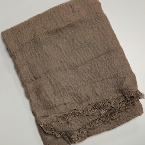 K&ouml;nnte beinhalten: Ein rechteckiger Schal in einem einfarbigen Taupe-Braun. Der Stoff weist durchgehend eine ausgepr&auml;gte, zerknitterte Textur auf. Die untere Kante des Schals ist mit einem ausgefransten Saum versehen, der dem Design ein haptisches Element verleiht.