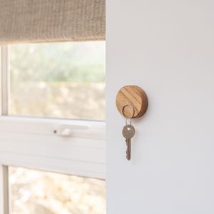 Peut inclure: Un porte-cl&eacute;s en bois rond avec un anneau m&eacute;tallique. Le porte-cl&eacute;s est fix&eacute; &agrave; un mur blanc.