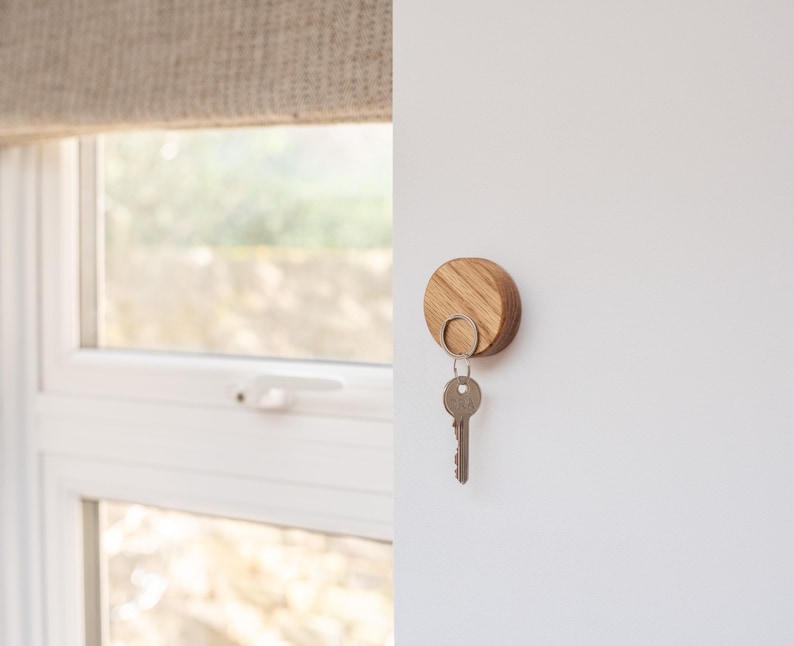 Peut inclure: Un porte-cl&eacute;s en bois rond avec un anneau m&eacute;tallique. Le porte-cl&eacute;s est fix&eacute; &agrave; un mur blanc.