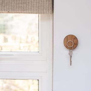 Peut inclure: Un porte-cl&eacute;s en bois rond avec un anneau pour cl&eacute;s. Le porte-cl&eacute;s est fix&eacute; &agrave; un mur blanc &agrave; c&ocirc;t&eacute; d'une fen&ecirc;tre.