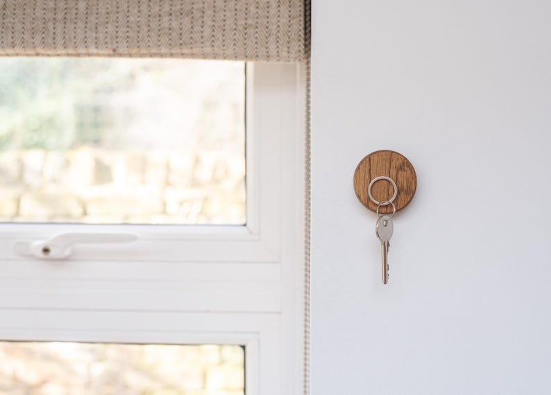 Peut inclure: Un porte-cl&eacute;s en bois rond avec un anneau pour cl&eacute;s. Le porte-cl&eacute;s est fix&eacute; &agrave; un mur blanc &agrave; c&ocirc;t&eacute; d'une fen&ecirc;tre.