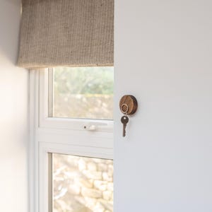 Peut inclure: Un porte-cl&eacute;s en bois avec un anneau m&eacute;tallique fix&eacute; &agrave; un mur blanc. Une cl&eacute; est accroch&eacute;e &agrave; l'anneau.